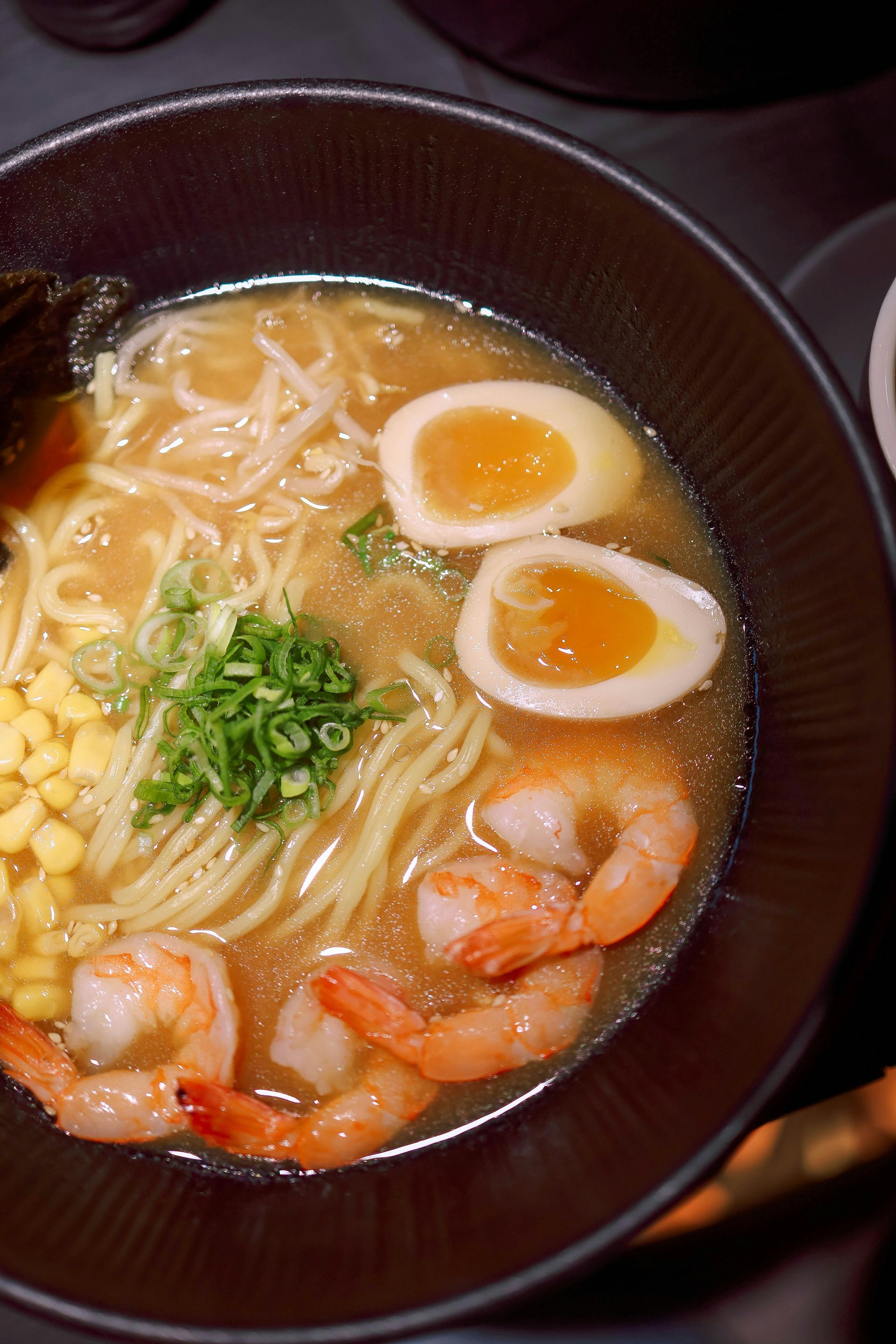 Ramen bowl with noodles, shrimp, corn, soft-boiled eggs, and green onions.
