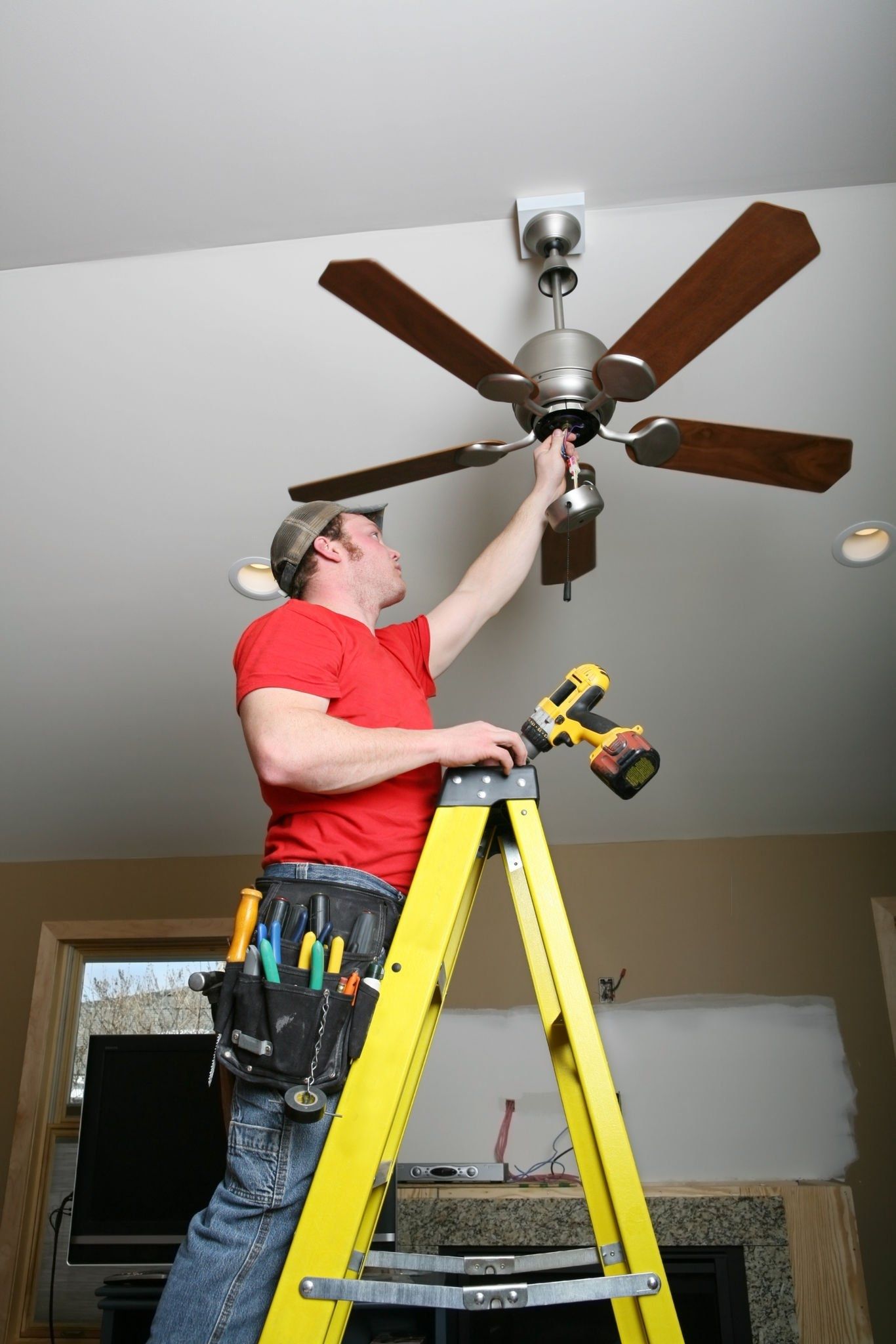A man is standing on a ladder fixing a ceiling fan.