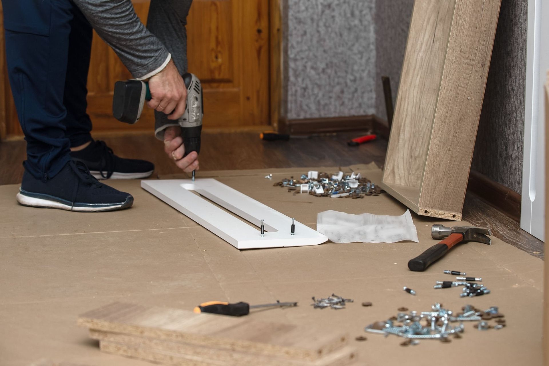 A man is using a drill to assemble a piece of furniture.