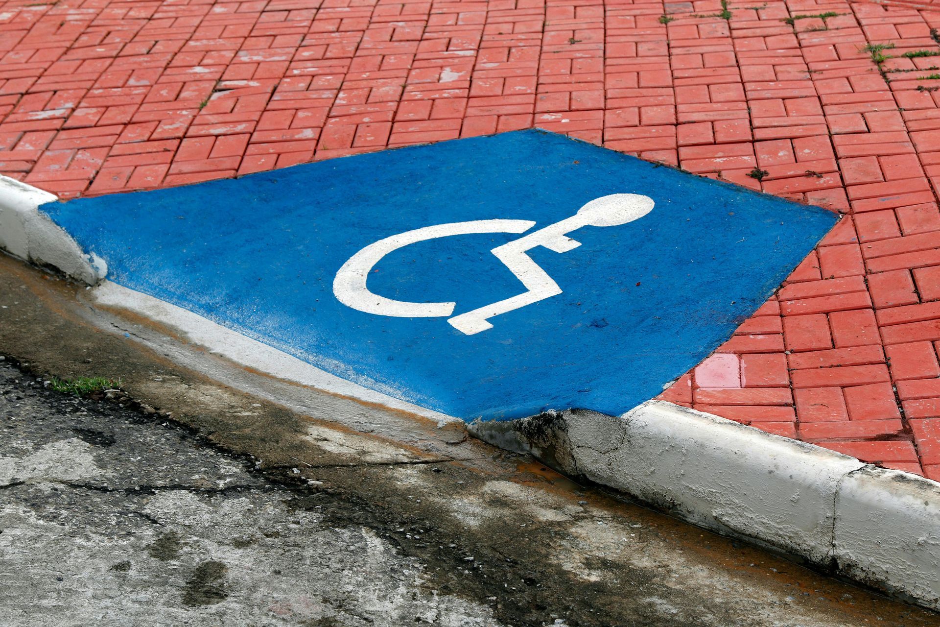 Marcações em azul e branco de vagas de estacionamento acessíveis em pavimento de tijolos vermelhos.