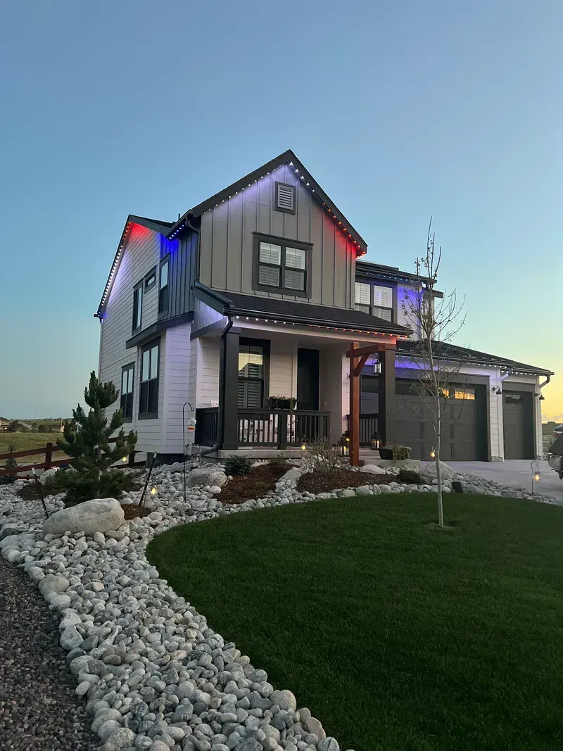 Two-story house with white siding and gray roof, illuminated with red and blue lights.