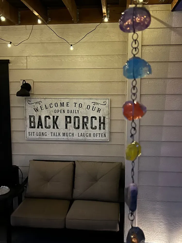 Back porch with seating, string lights, a sign, and a decorative rain chain.