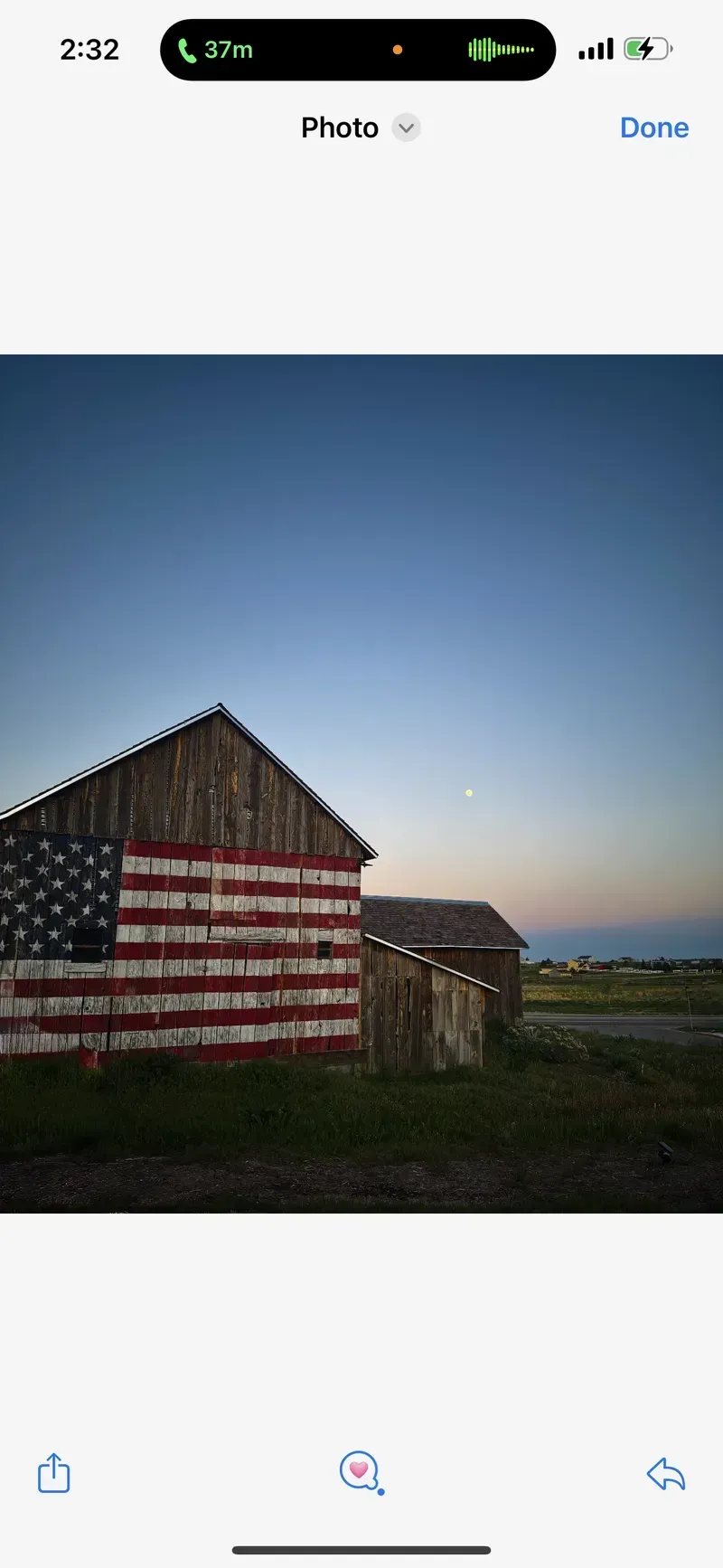 Barn painted with the American flag stands in a field. Evening sky and a second barn are also visible.