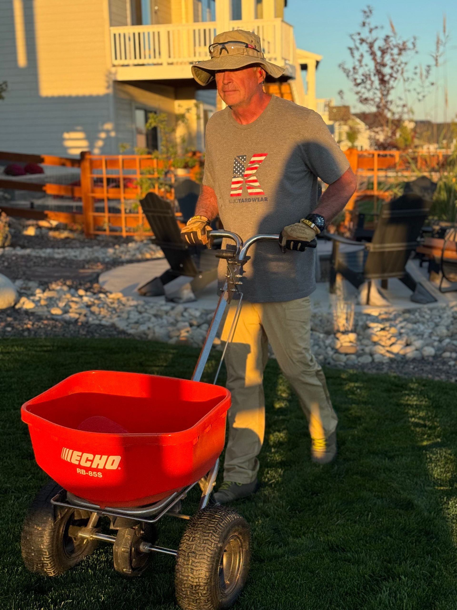 Person raking leaves into a bag on a lawn, wearing green gloves and a light green shirt.