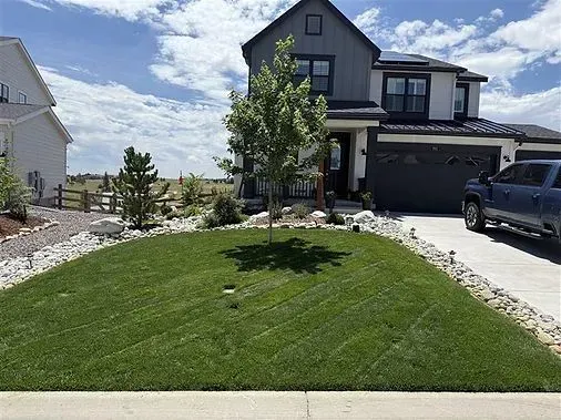 Two-story house with a manicured lawn, tree, and driveway; blue pickup truck parked in front.