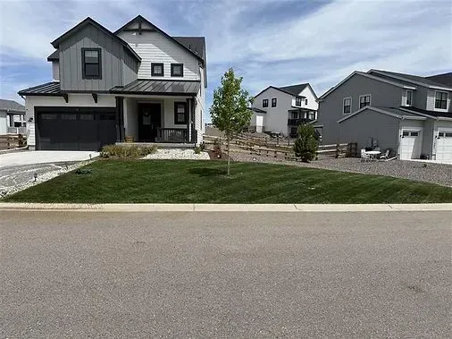 Two-story house with black and white exterior and a green lawn. Other houses are in the background.
