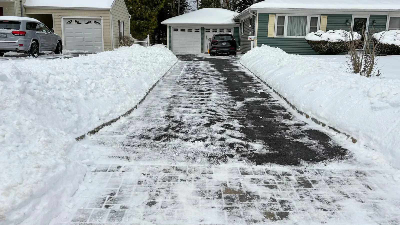 Snow-covered driveway cleared of snow. Snow banks line the driveway. Houses visible.