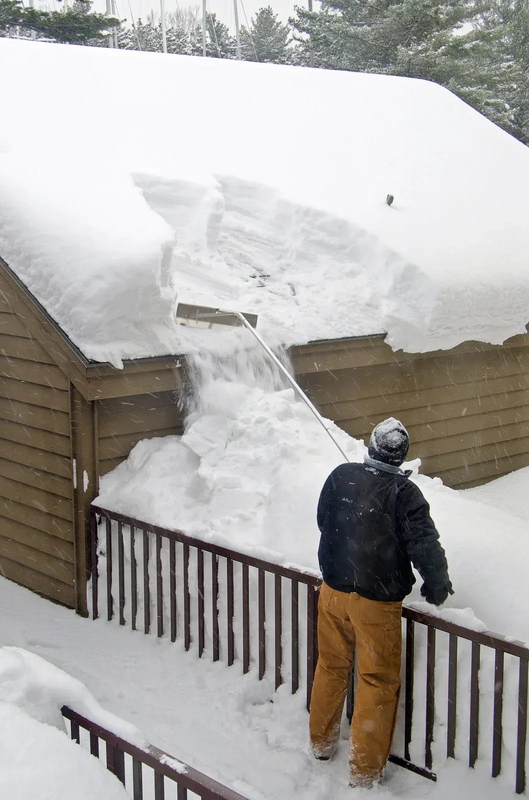 Person using an orange snowblower to clear snow from a sidewalk in front of a house.