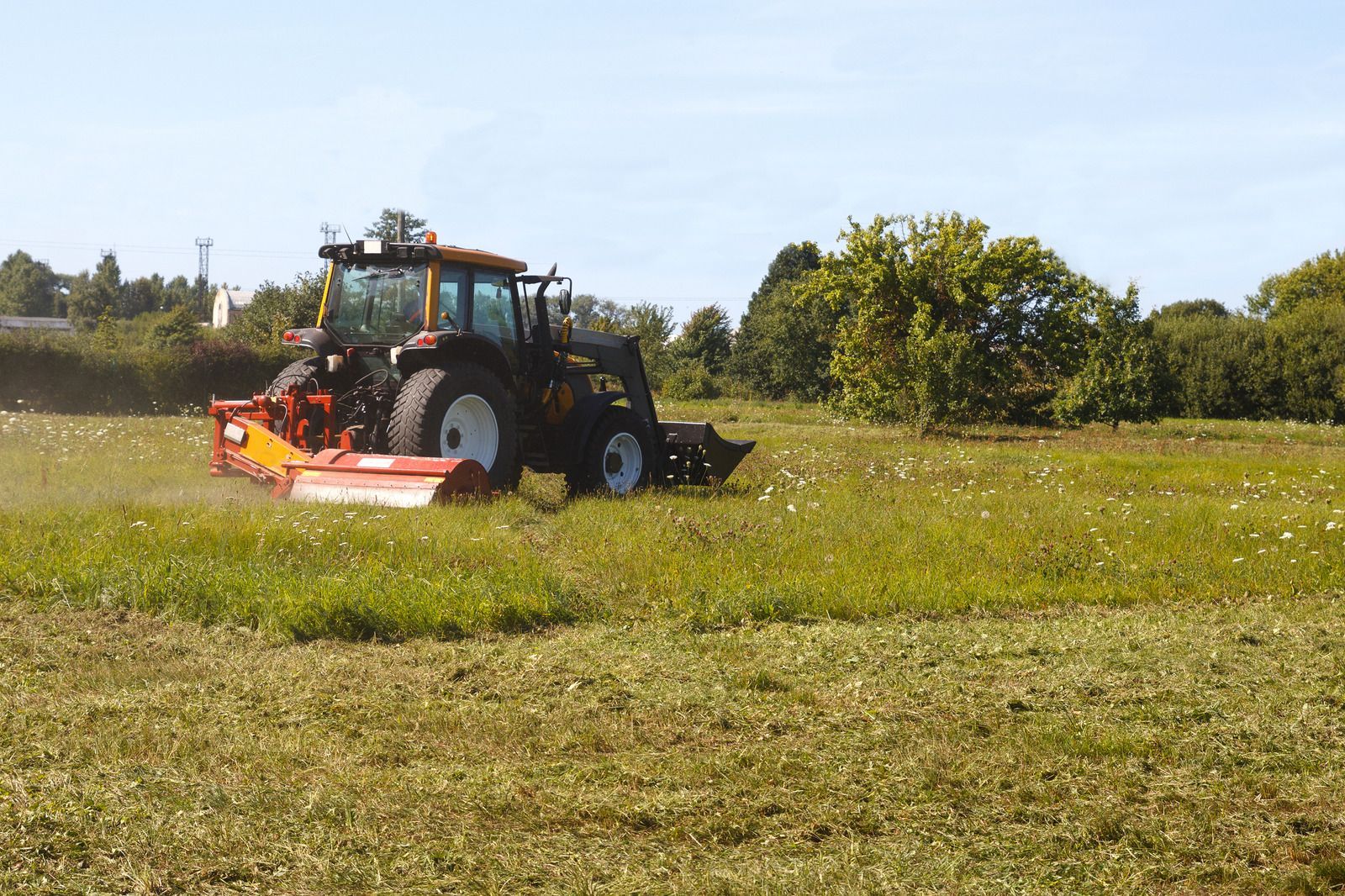 A tractor mowing a grassy field under a bright blue sky.