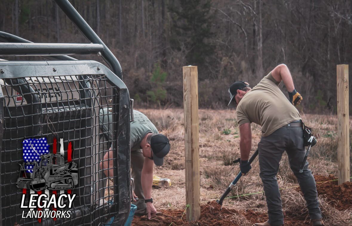 Two men are working on a fence in a field.