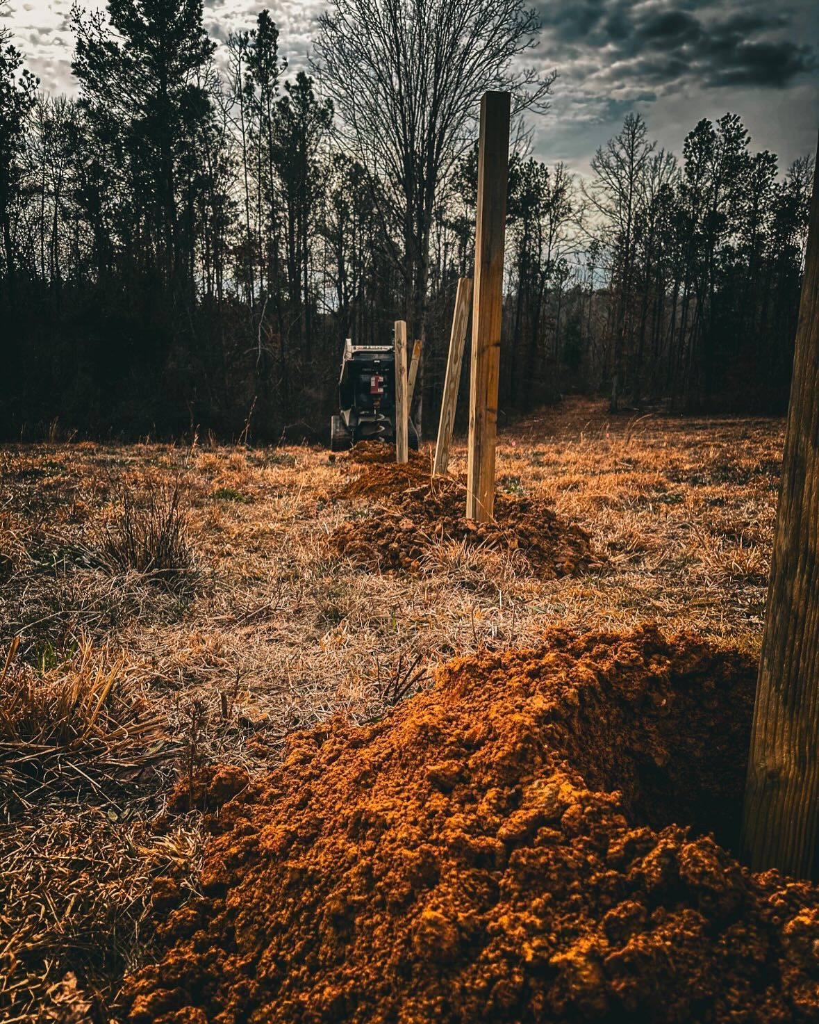 A fence is being built in a field with trees in the background.