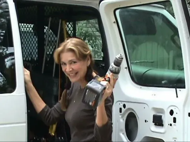 A woman is holding a drill in front of a white van