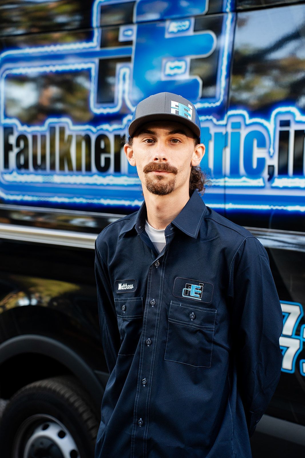 A man with a beard is wearing a baseball cap and a blue shirt.