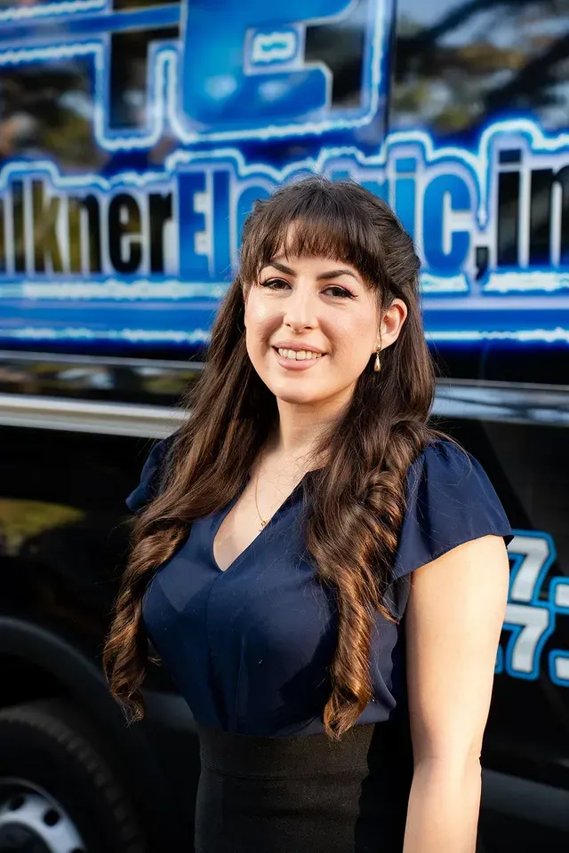 Faulkner Electric Office Coordinator, Michelle Mandarin, in front of our work vans with Faulkner Electric Logo