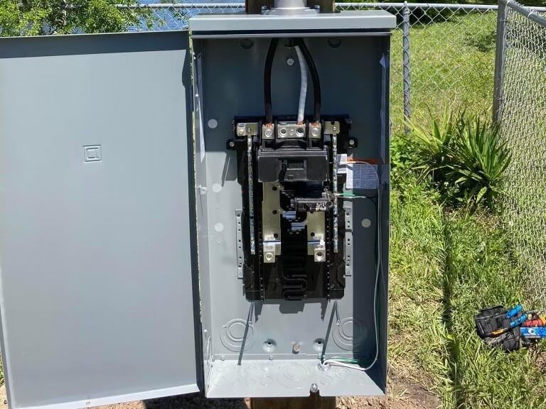 A electrical box is sitting on top of a pole in the grass.