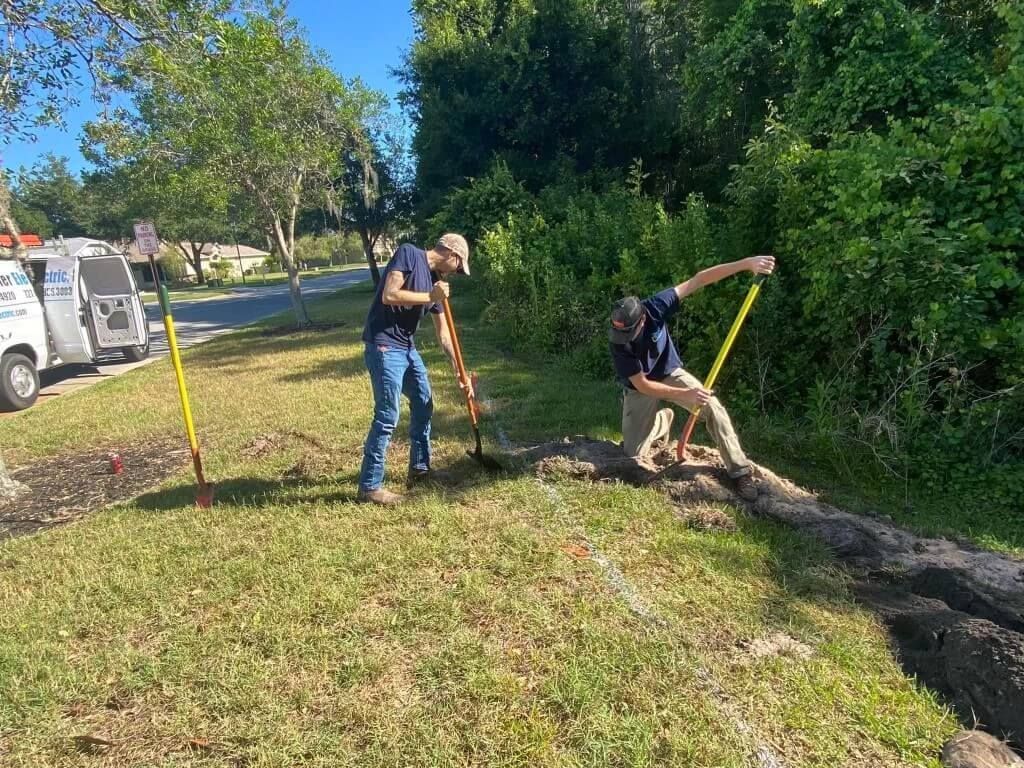 Two men are digging a hole in the grass with shovels.