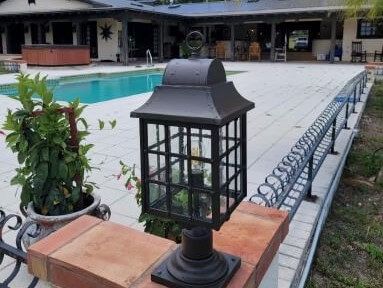 A lantern is sitting on a brick post in front of a swimming pool.