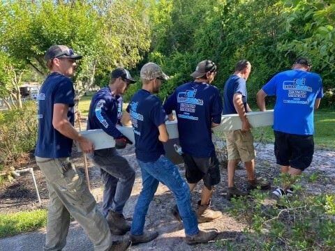 A group of men wearing blue shirts are carrying buckets.