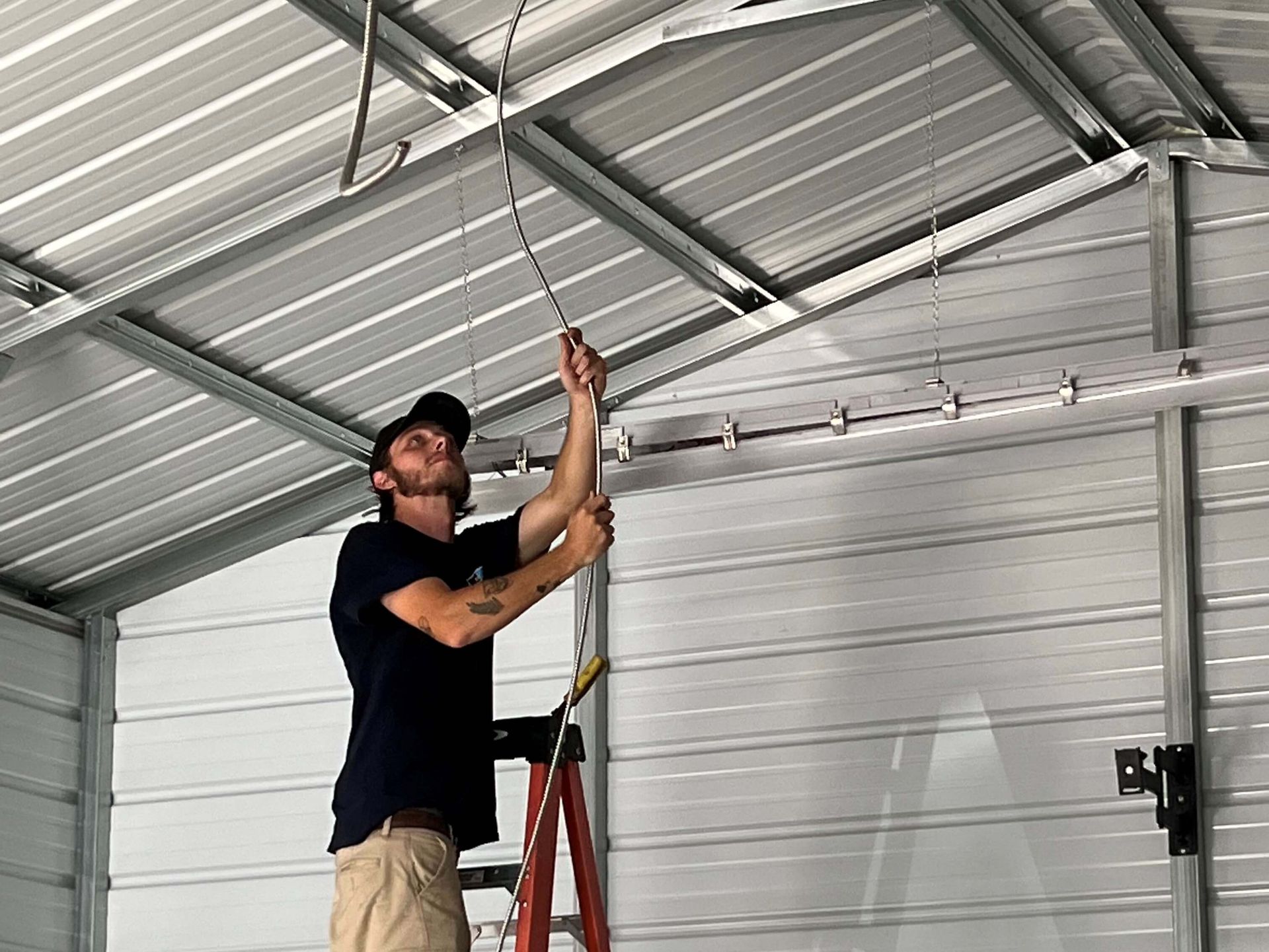 A man is standing on a ladder working on a garage door.
