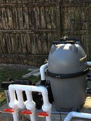 A swimming pool filter is sitting next to a wooden fence.