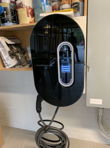 Un chargeur de voiture électrique noir se trouve à côté d'une étagère dans un garage.