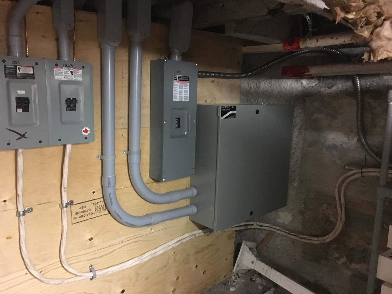 Un tas de coffrets électriques sont accrochés à un mur dans un sous-sol.