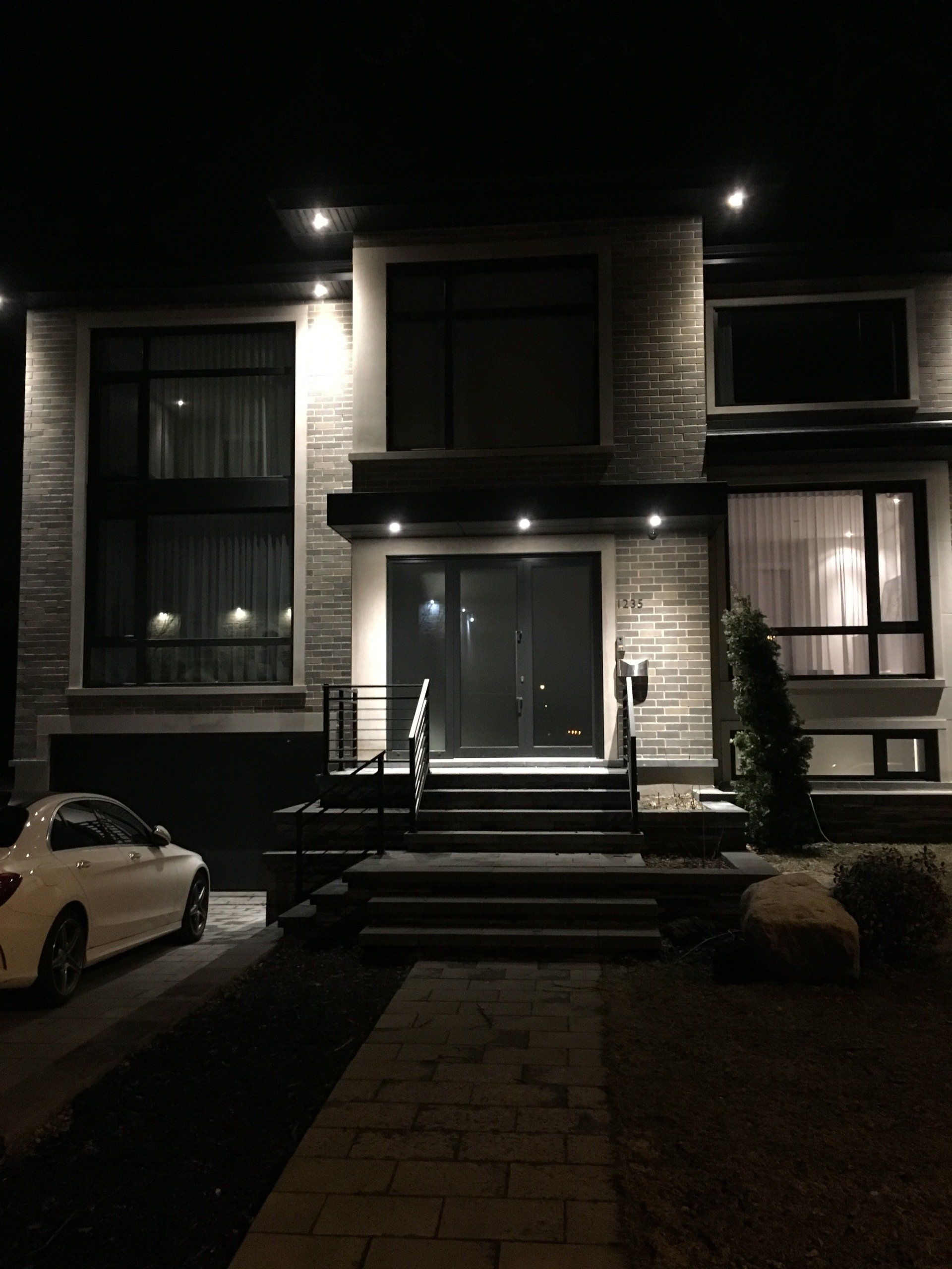 Une voiture blanche est garée devant une maison la nuit