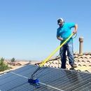 A man is cleaning solar panels on the roof of a house.