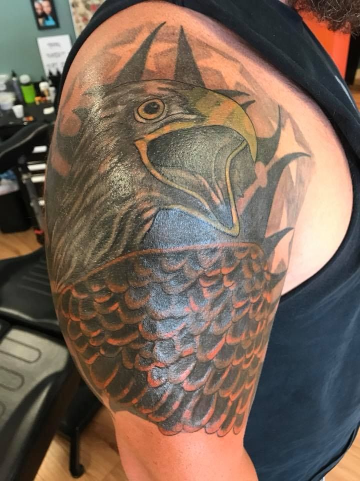 Large raven tattoo on a person's shoulder and upper arm in black and orange tones