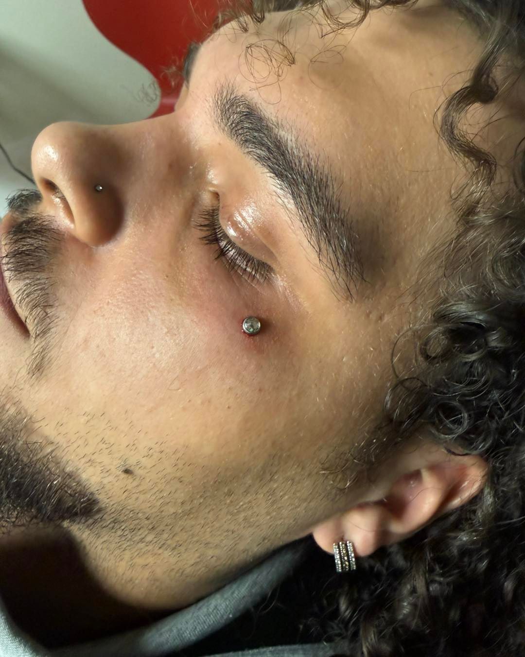 Close-up profile of a person with curly hair and a nose ring, resting their face on a hand.