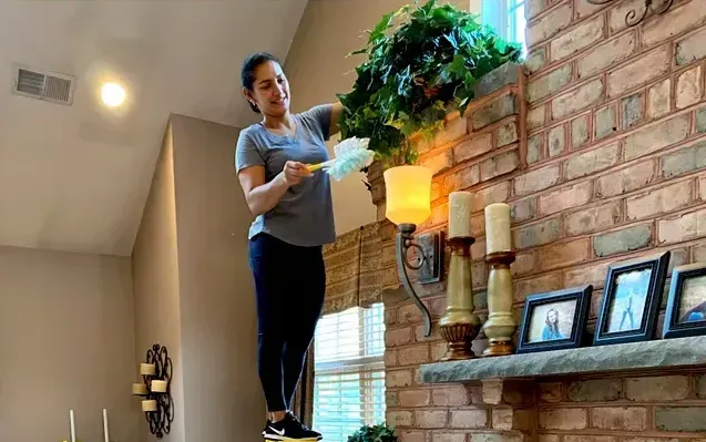 Amaya's Cleaning Service - A woman is standing on a shelf in a living room holding a plant.