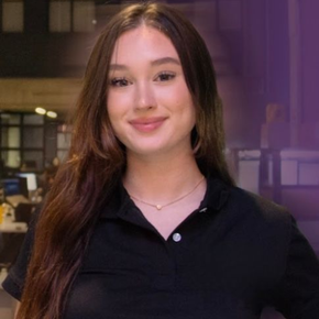 Woman with long brown hair, smiling, wearing a black polo shirt and necklace, in an office setting.
