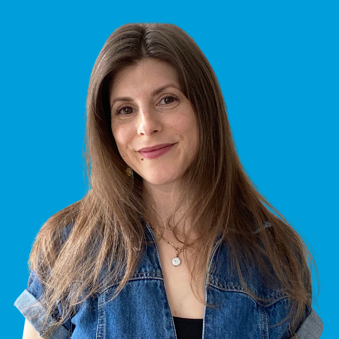 Woman with long brown hair wearing a denim jacket, looking at the camera.