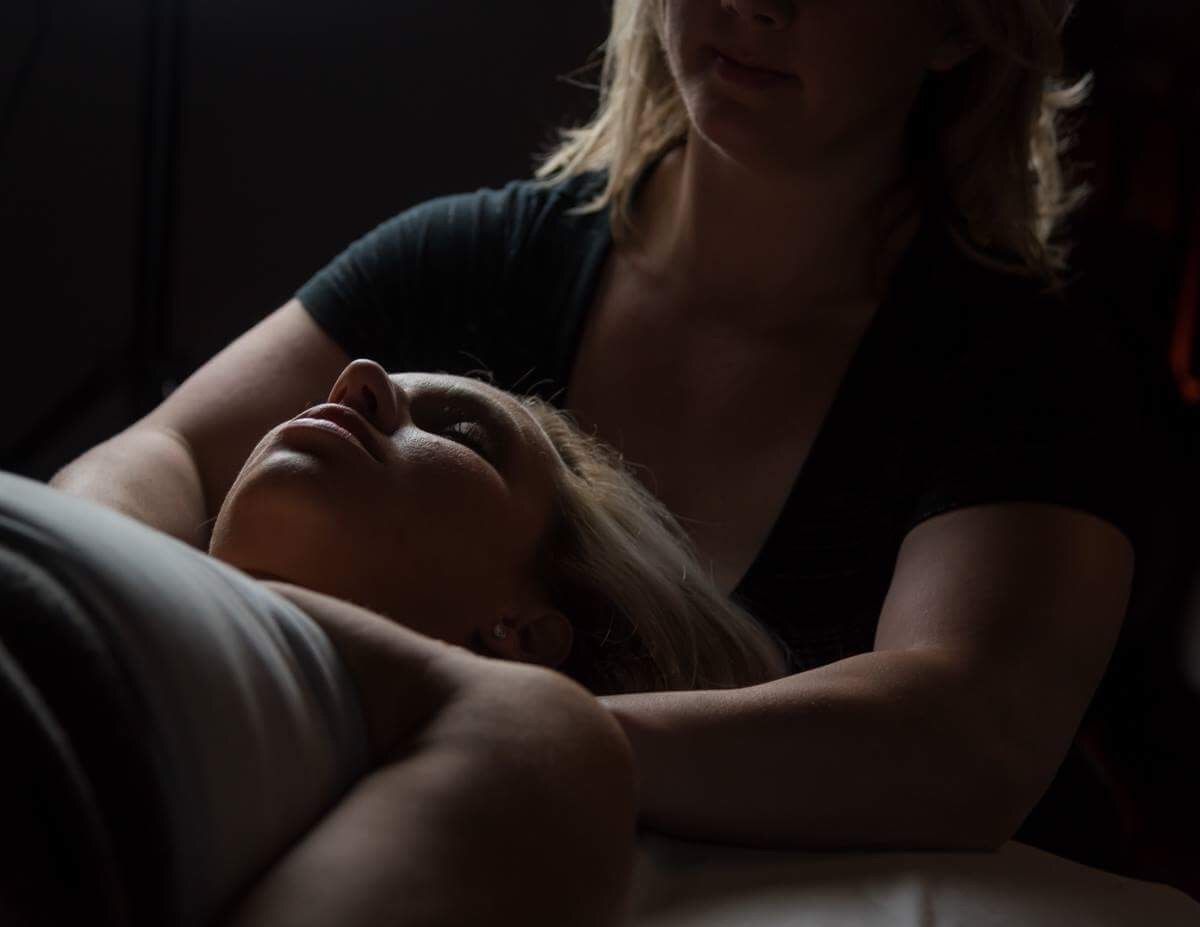 A woman is giving a massage to a woman laying on a bed.