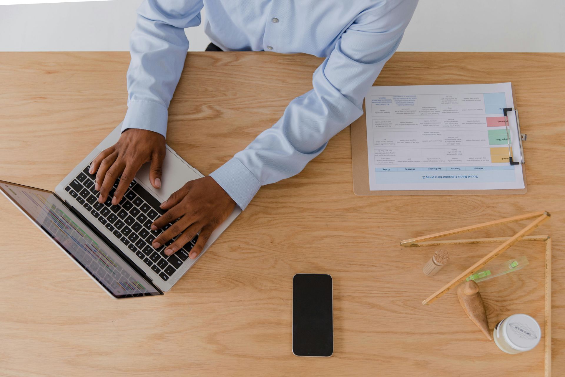 Person typing on a laptop at a wooden desk with papers, pencils, and a phone nearby