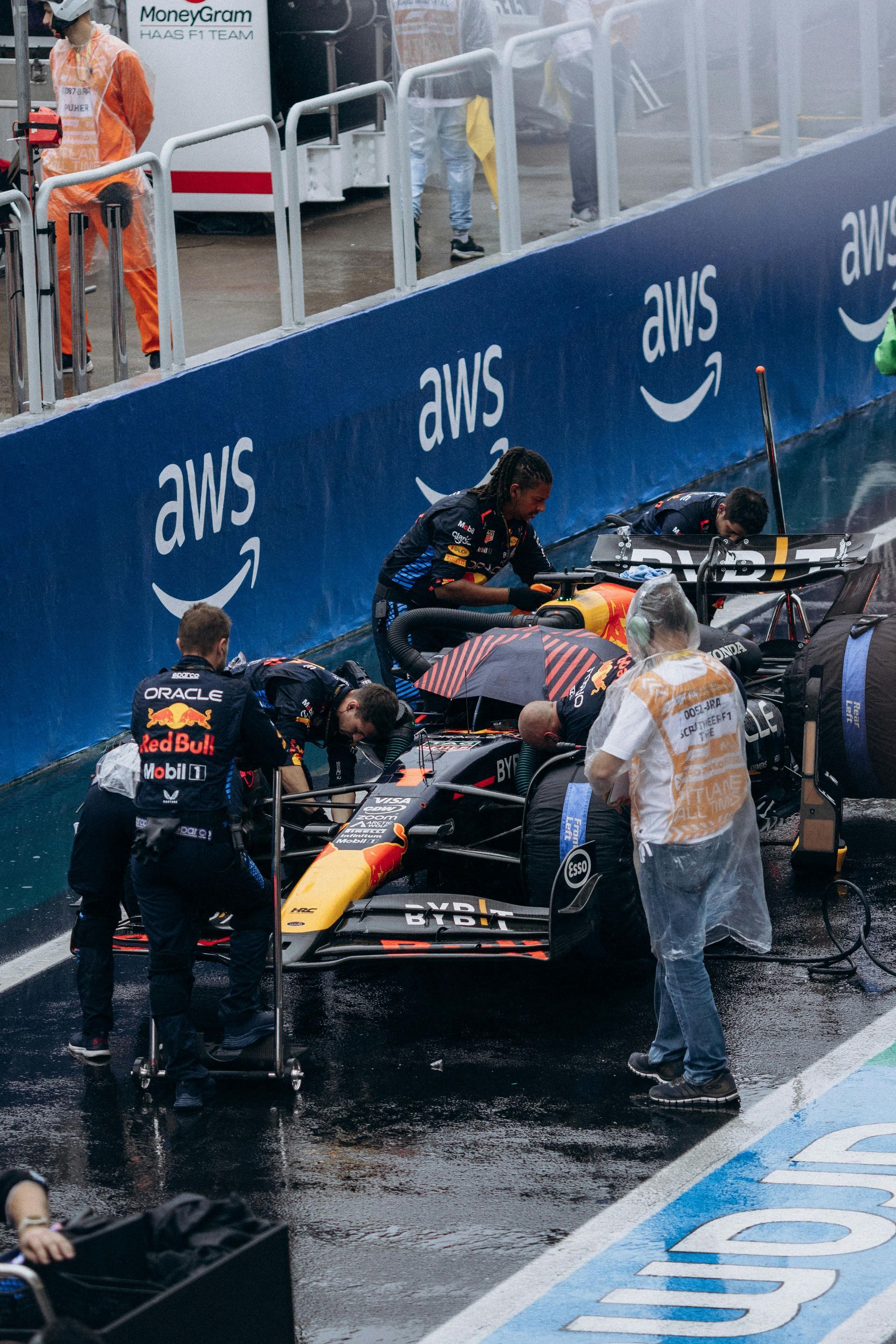 Red Bull Formula 1 car in the pit lane, crew working, wet track, AWS signage.