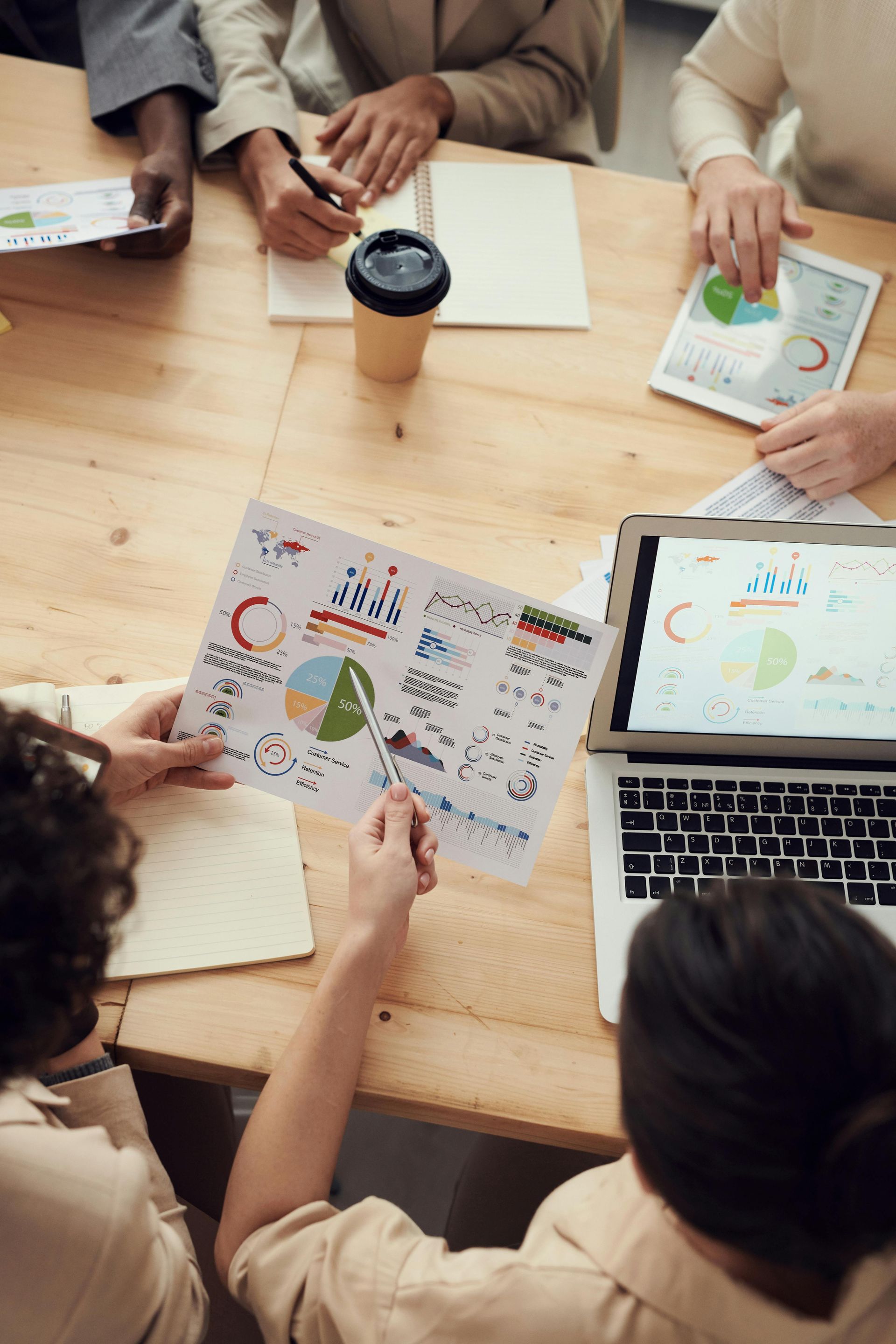 People collaborating around a wooden table with charts, notebooks, and a laptop in a meeting.