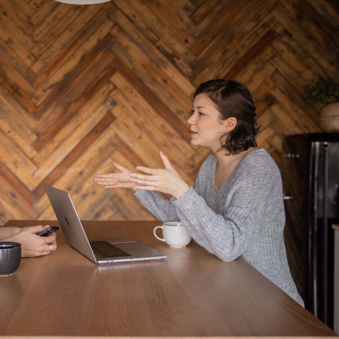 Two women are sitting at a table with a laptop and a cup of coffee