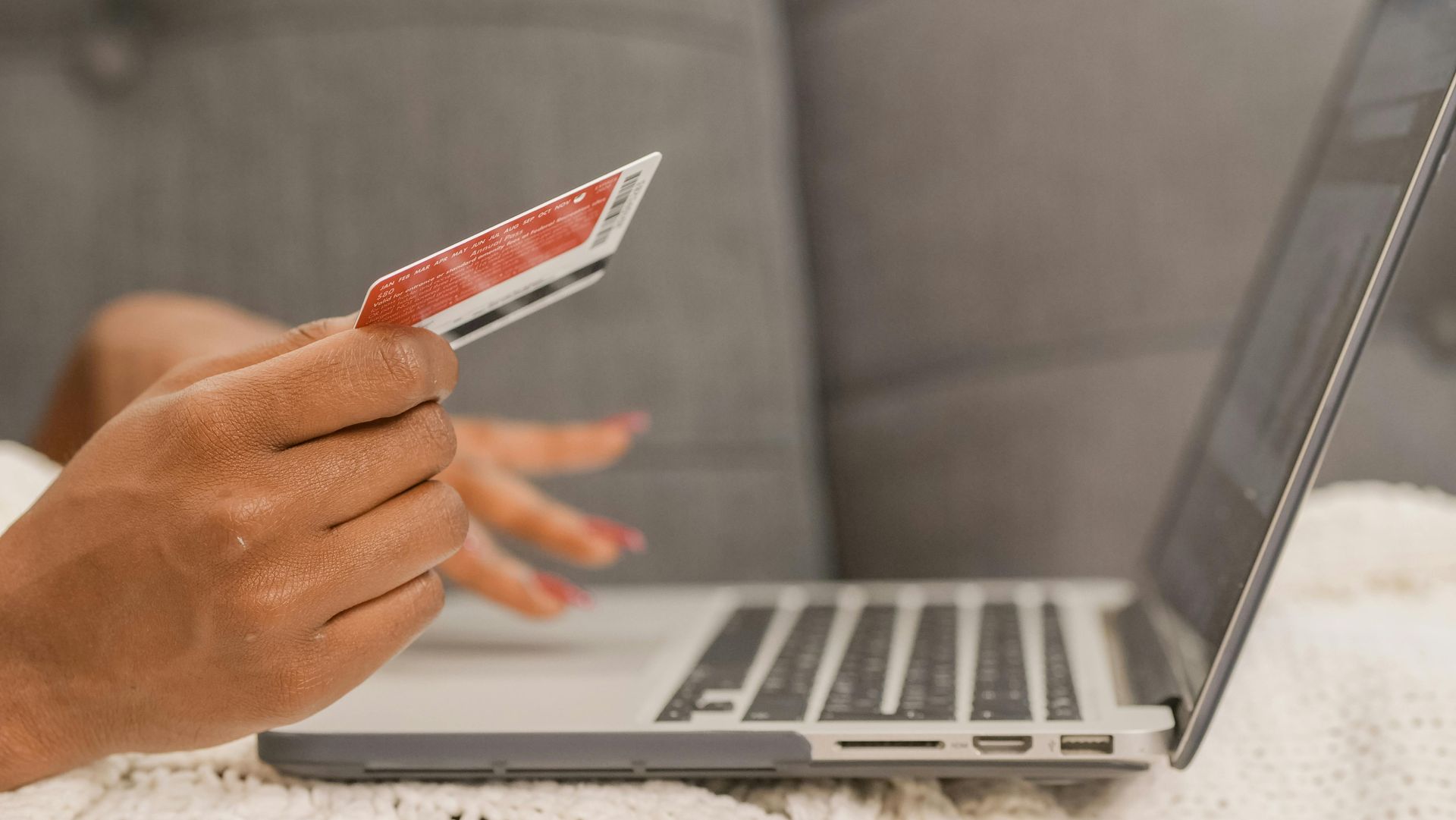 Hand holding a credit card near a laptop on a white table