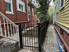 A black fence is surrounding a sidewalk between two buildings.