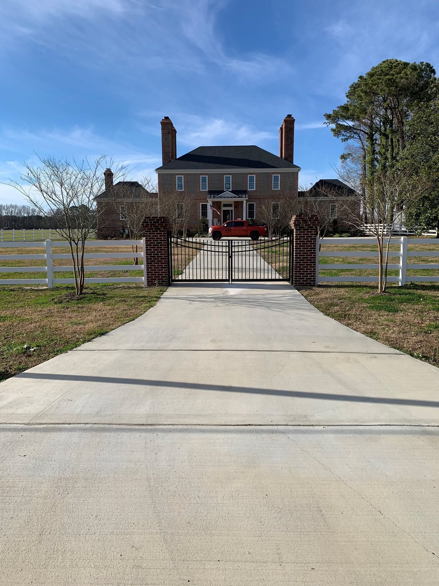 A driveway leading to a large house with a white fence