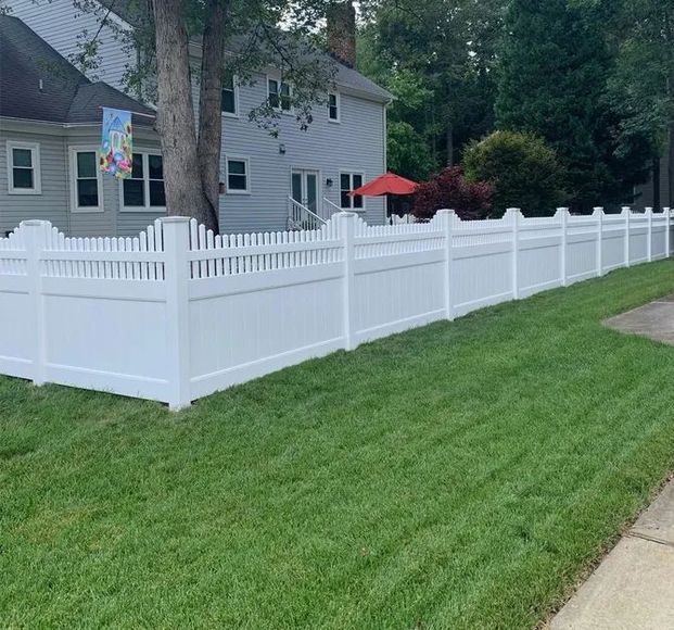 A white picket fence surrounds a lush green lawn in front of a house.