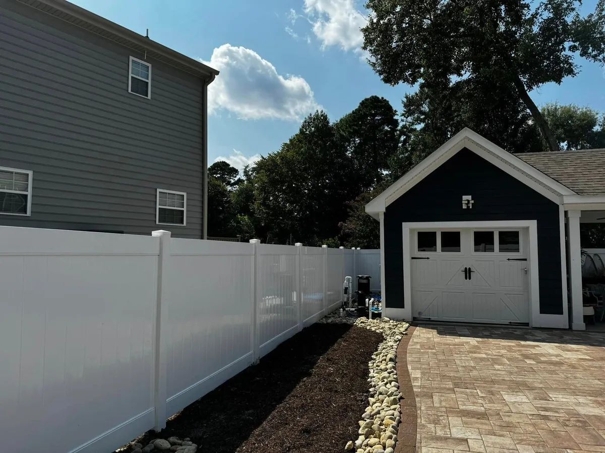 A white fence surrounds a garage next to a house.