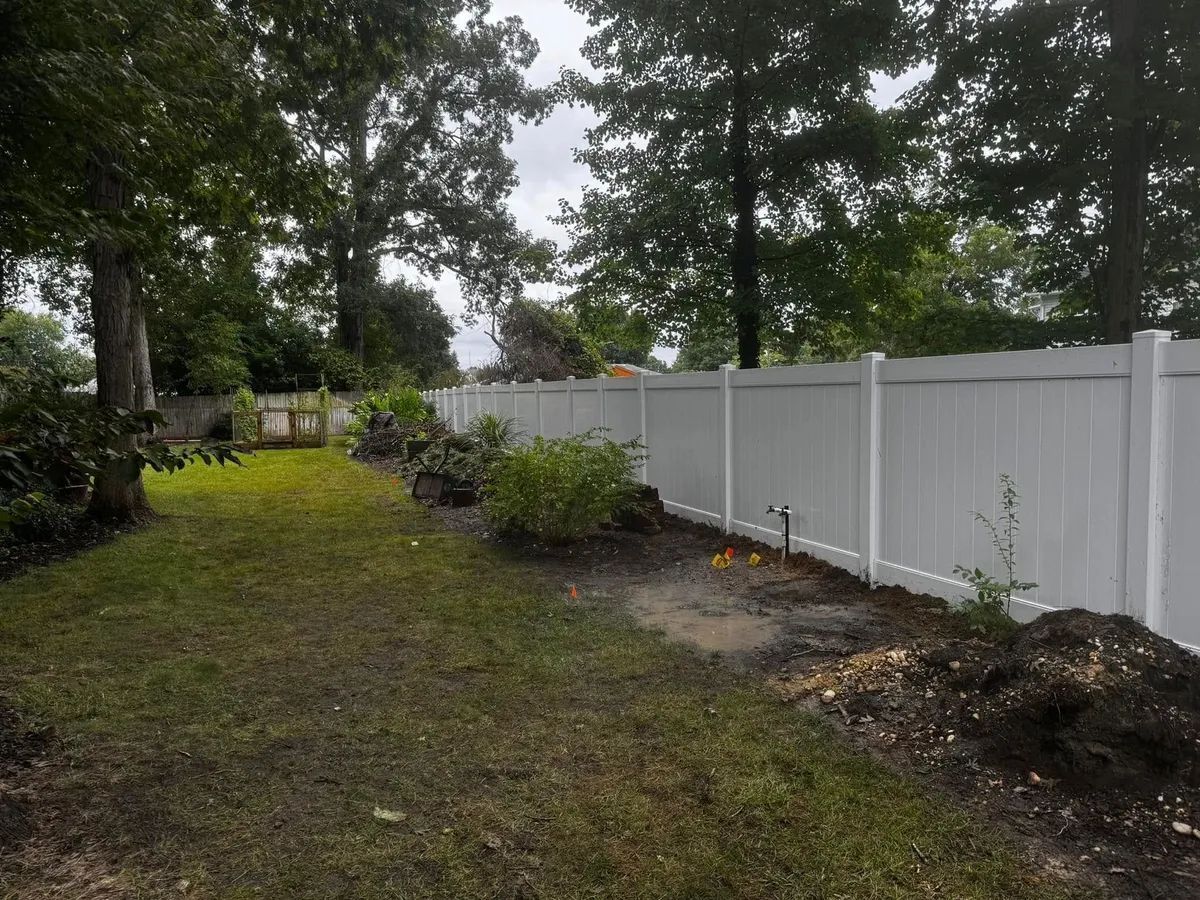 A white fence surrounds a backyard filled with grass and trees.