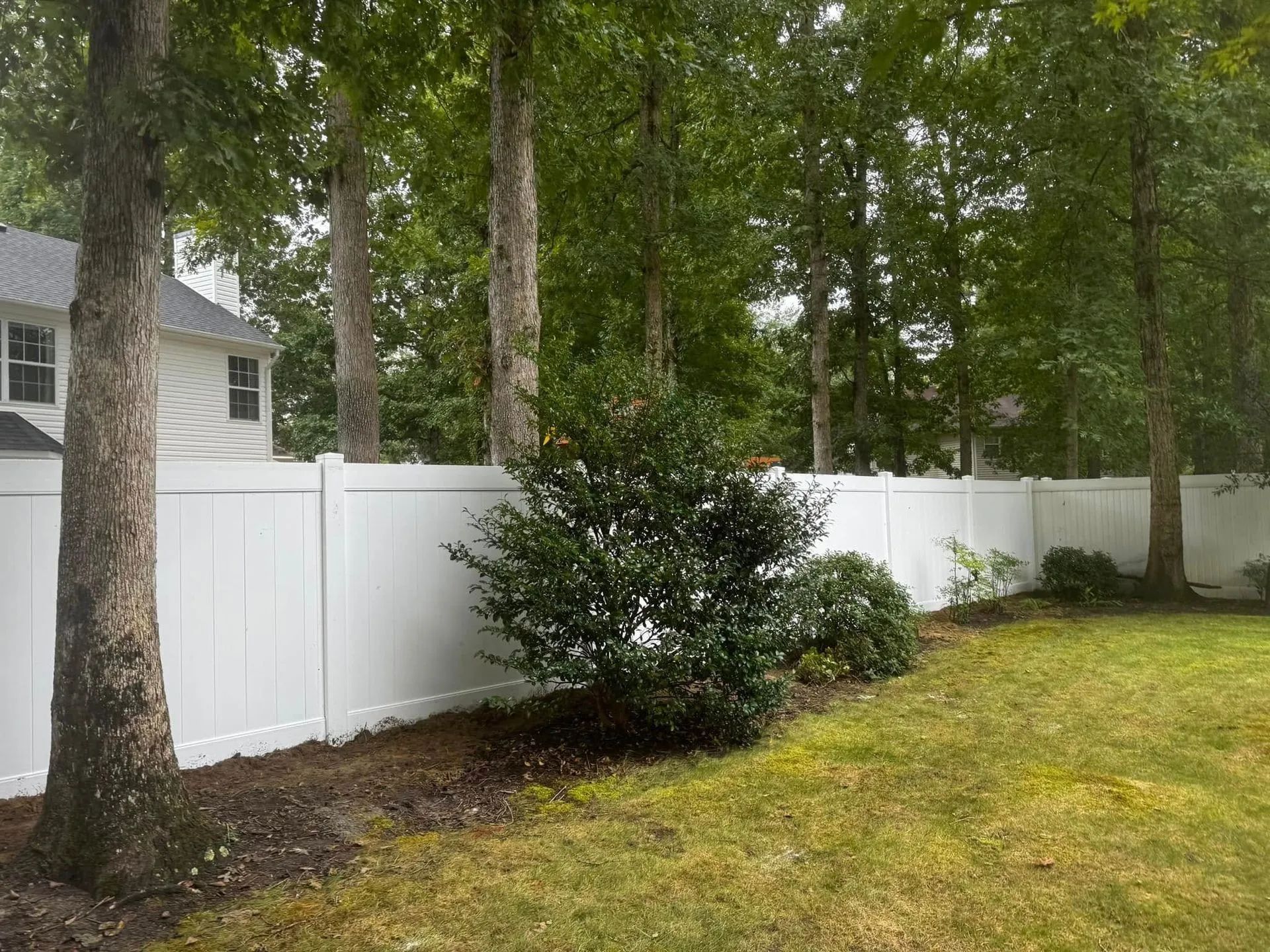 A white fence is surrounded by trees in a backyard.