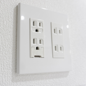 White duplex electrical outlets on a glossy wall plate against a textured white wall