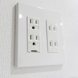 White duplex electrical outlets on a glossy wall plate against a textured white wall