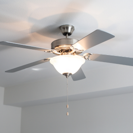Silver ceiling fan with light fixture and pull chain on a white ceiling