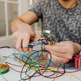 Hands wiring a colorful tangle of electronics on a table with tools and components