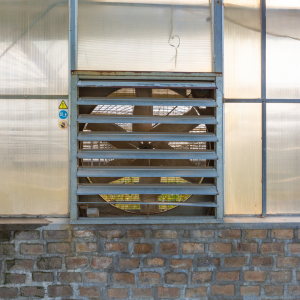 Louvered metal vent set into a brick wall beneath translucent greenhouse panels